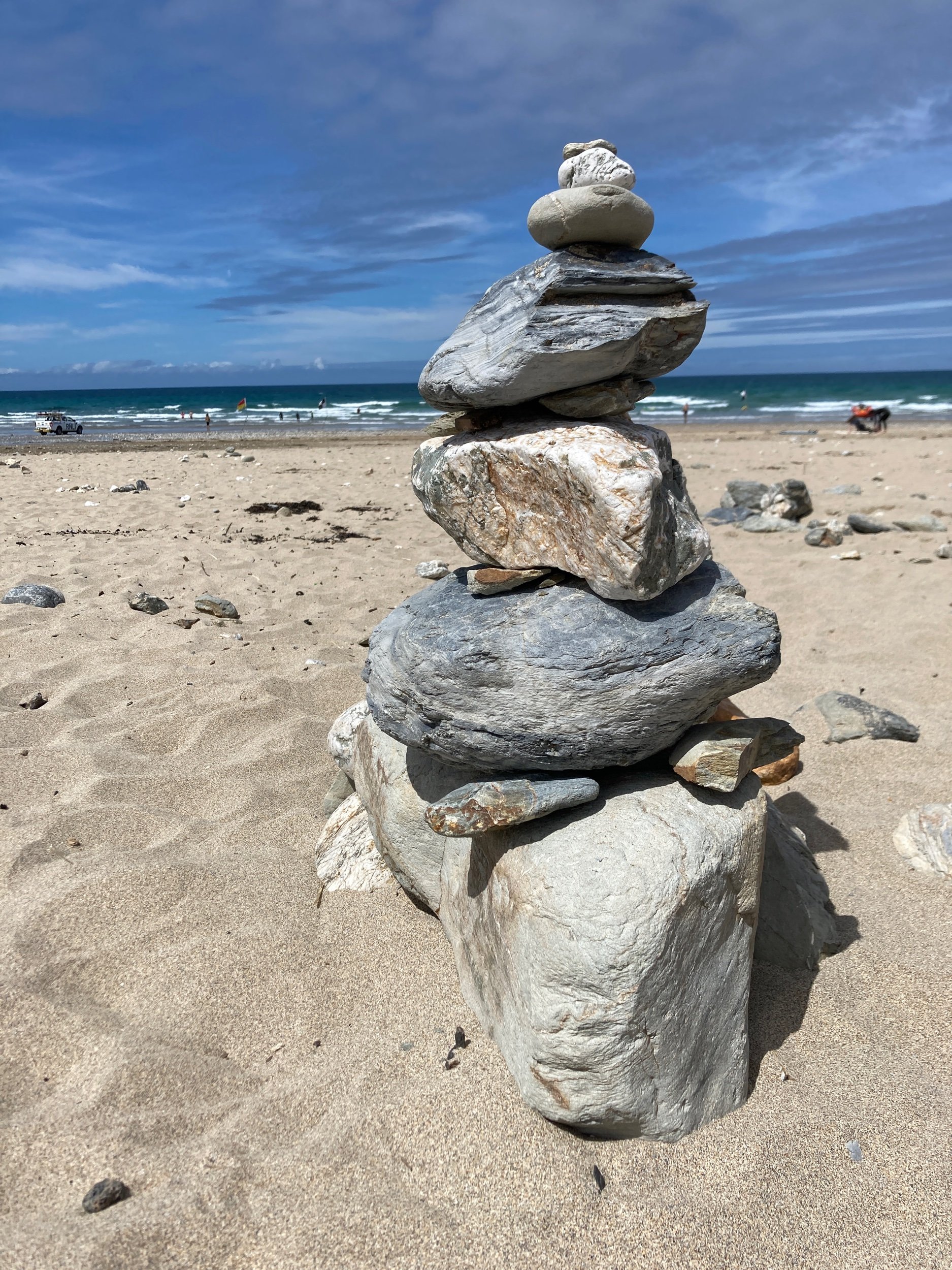 Pebbles stacked up on a beach to create a structure. The sand is soft, the sky is blue and there is an imperfection to the structure that makes it look different to a regular image of pebbles balancing.